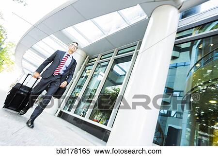 Mixed race businessman rolling luggage in office View Large Photo Image Stock Photography - Mixed race businessman rolling luggage in office. Fotosearch