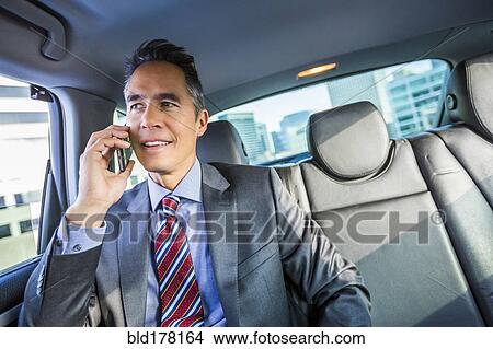 Picture - Mixed race businessman talking on cell phone in car. Fotosearch