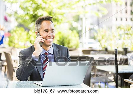 Stock Photo - Mixed race businessman talking on cell phone in cafe. Fotosearch