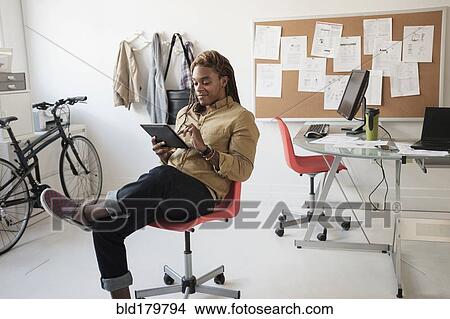 Picture - Mixed race businessman using digital tablet in office. Fotosearch