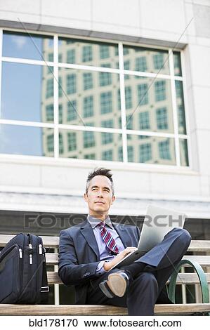 Stock Image - Mixed race businessman using laptop outdoors. Fotosearch