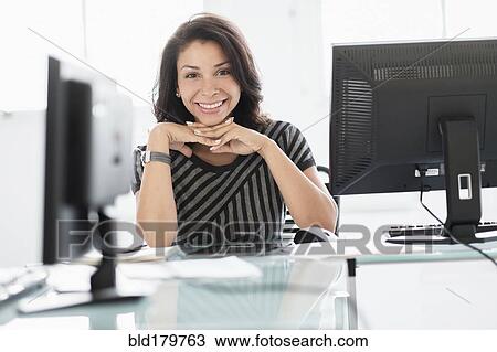 Stock Image - Mixed race businesswoman smiling at desk. Fotosearch