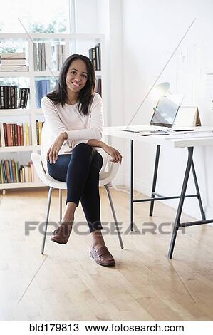 Stock Image - Mixed race businesswoman smiling in home office. Fotosearch