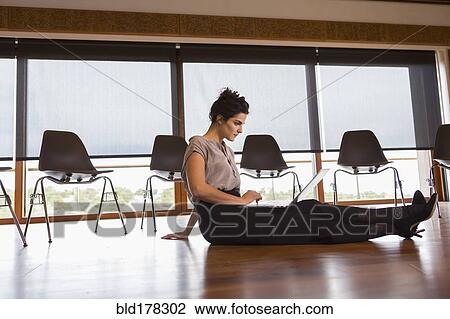 Stock Image - Mixed race businesswoman using laptop on floor of meeting room. Fotosearch