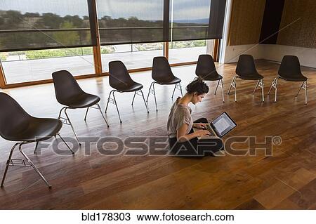 Stock Image - Mixed race businesswoman using laptop on floor of meeting room. Fotosearch