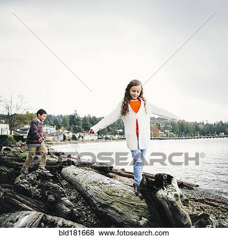 Stock Photo - Mixed race children climbing on logs at lake. Fotosearch