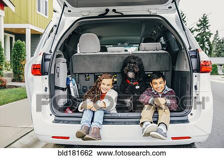 Stock Image - Mixed race children sitting with dog in car hatch. Fotosearch