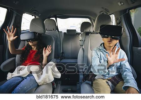 Stock Photography - Mixed race children using virtual reality goggles in car. Fotosearch