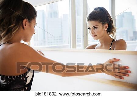 Stock Image - Mixed race dancer examining herself in mirror. Fotosearch