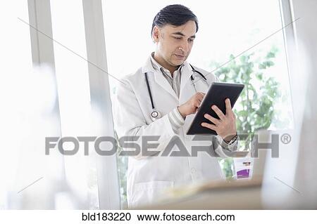 Stock Image - Mixed race doctor using digital tablet. Fotosearch