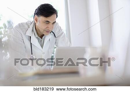 Stock Photo - Mixed race doctor working on laptop. Fotosearch