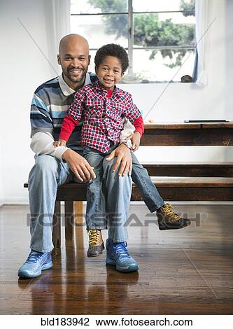 Stock Image - Mixed race father and son smiling at table. Fotosearch