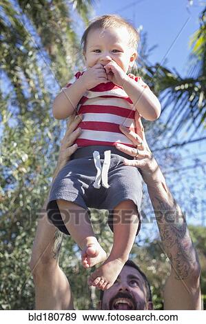 Stock Photo - Mixed race father holding baby outdoors. Fotosearch
