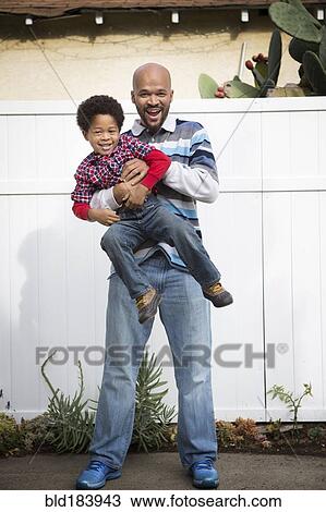 Stock Image - Mixed race father holding son outdoors. Fotosearch