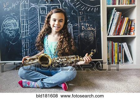 Stock Photo - Mixed race girl holding saxophone on floor. Fotosearch