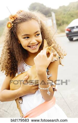 Stock Image - Mixed race girl petting dog outdoors. Fotosearch