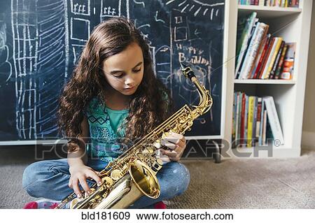 Stock Photo - Mixed race girl playing saxophone on floor. Fotosearch
