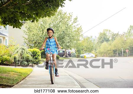 Stock Photo - Mixed race girl riding bicycle on sidewalk. Fotosearch