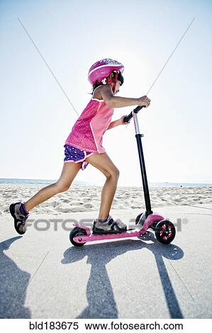 Stock Photography - Mixed race girl riding scooter at beach. Fotosearch