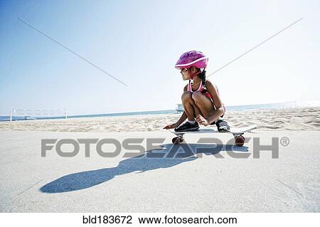 Stock Image - Mixed race girl riding skateboard at beach. Fotosearch
