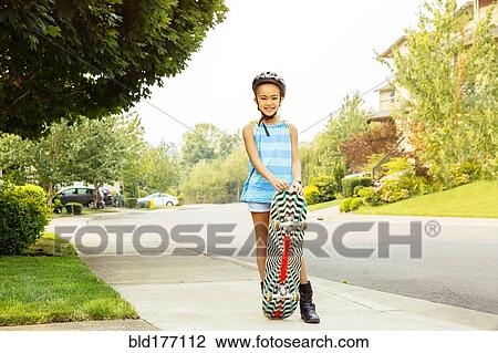 Stock Image - Mixed race girl riding skateboard on sidewalk. Fotosearch