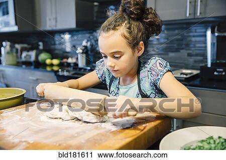 Stock Image - Mixed race girl rolling dough in kitchen. Fotosearch