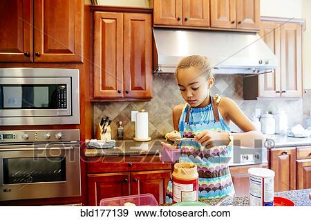 Stock Photo - Mixed race girl scooping peanut butter in kitchen. Fotosearch