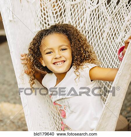 Stock Image - Mixed race girl sitting in hammock. Fotosearch
