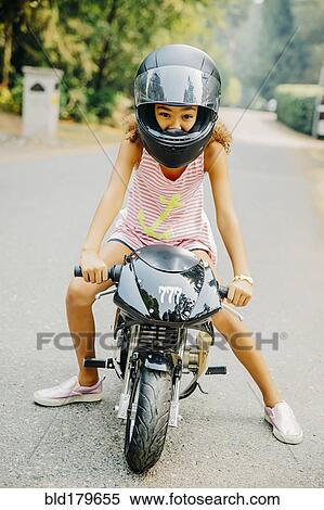 Stock Photography - Mixed race girl sitting on miniature motorcycle. Fotosearch