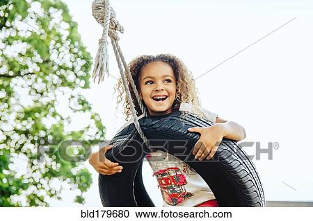 Stock Image - Mixed race girl smiling in tire swing. Fotosearch