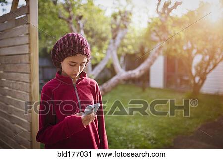 Stock Image - Mixed race girl using cell phone in backyard. Fotosearch