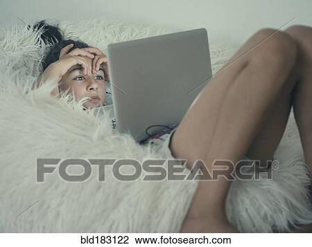 Stock Image - Mixed race girl using laptop in beanbag chair. Fotosearch