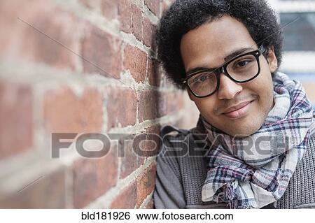 Stock Photograph - Mixed race man leaning on brick wall. Fotosearch