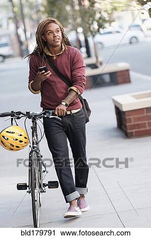 Stock Image - Mixed race man pushing bicycle outdoors. Fotosearch