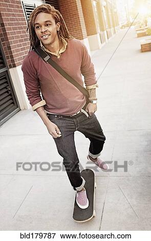 Stock Photo - Mixed race man riding skateboard on sidewalk. Fotosearch