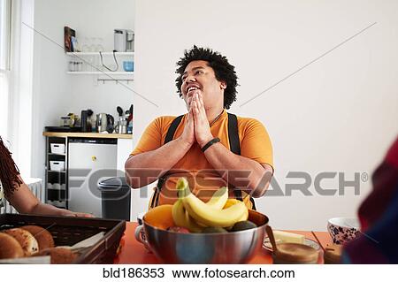 Stock Image - Mixed race man sitting at table and praying. Fotosearch