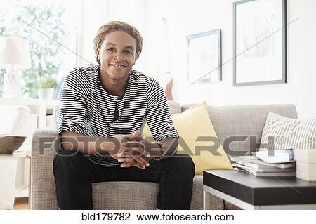 Stock Image - Mixed race man sitting on sofa. Fotosearch