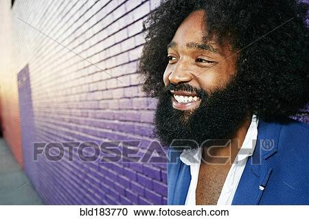 Stock Image - Mixed race man smiling outdoors near purple wall. Fotosearch