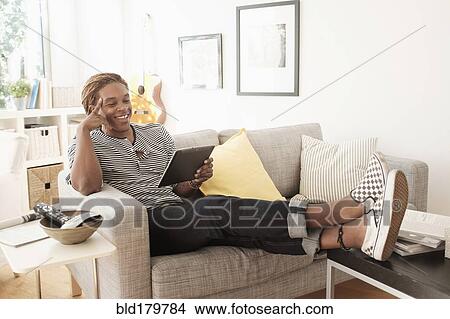 Mixed race man using digital tablet on sofa View Large Photo Image Picture - Mixed race man using digital tablet on sofa. Fotosearch