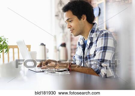 Stock Image - Mixed race man using laptop in coffee shop. Fotosearch