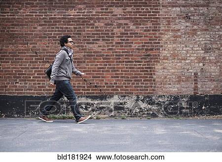 Picture - Mixed race man walking near brick wall. Fotosearch