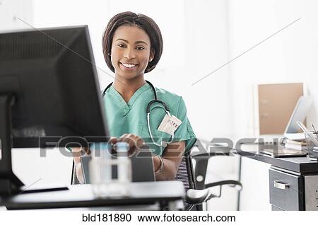 Stock Image - Mixed race nurse smiling at computer. Fotosearch
