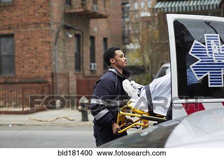 Stock Image - Mixed race paramedic loading patient into ambulance. Fotosearch