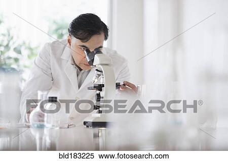 Stock Photography - Mixed race scientist using microscope in laboratory. Fotosearch