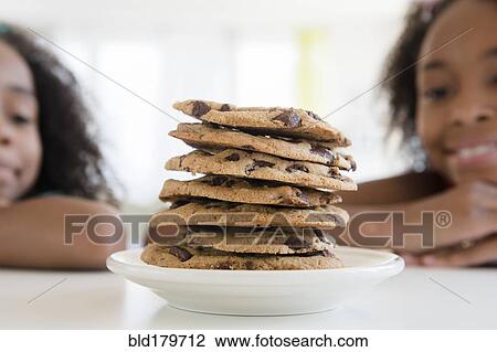 Stock Image - Mixed race sisters admiring stack of cookies. Fotosearch
