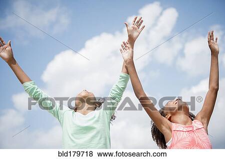 Mixed race sisters cheering in blue sky View Large Photo Image Stock Photo - Mixed race sisters cheering in blue sky. Fotosearch
