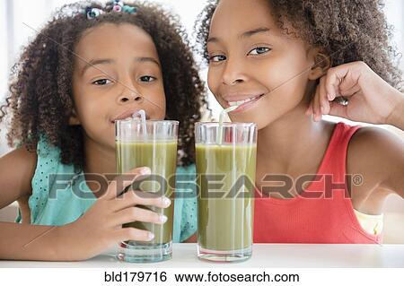 Stock Photograph - Mixed race sisters drinking healthy juice. Fotosearch