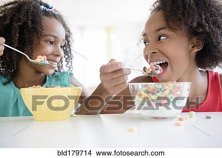Picture - Mixed race sisters eating cereal. Fotosearch