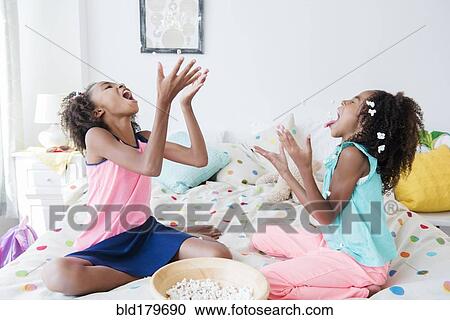 Mixed race sisters eating popcorn on bed View Large Photo Image Stock Image - Mixed race sisters eating popcorn on bed. Fotosearch