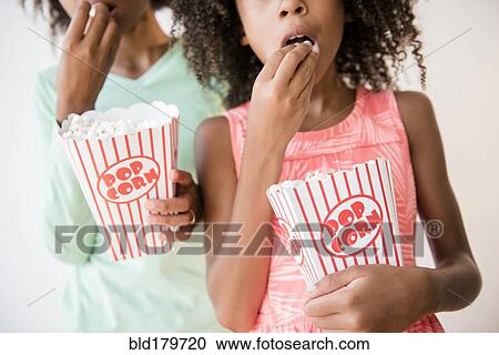 Mixed race sisters eating popcorn View Large Photo Image Stock Image - Mixed race sisters eating popcorn. Fotosearch